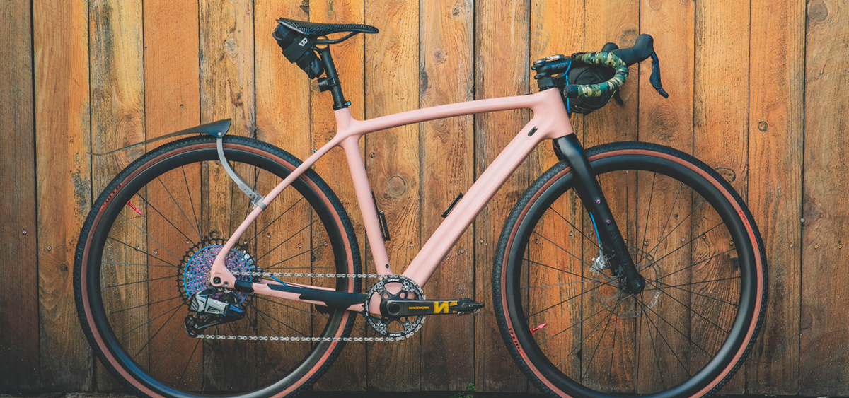 A pink road bicycle parked against a wooden wall